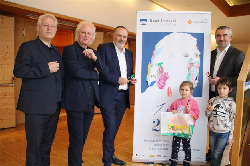 Die Liszt Festival-Intendanten Eduard und Johannes Kutrowatz, Landeshauptmann Hans Peter Doskozil und Landesrat Heinrich Dorner freuen sich über den kreativen Beitrag der Raidinger Volksschüler wie Sophia und Georg, die Zeichnungen über Franz Liszt zu Papier brachten und so für eine farbenfrohe Galerie am Bauzaun der aktuellen Baustelle für die Erweiterung des Lisztzentrums setzten.