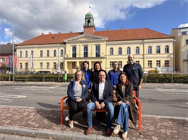 Gemeinsam ein Zeichen gegen Gewalt an Frauen und Mädchen setzen: Bürgermeister Georg Rosner mit Vertreterinnen des Soroptimist International Clubs Südburgenland/Stegersbach sowie den an der Herstellung beteiligten jungen Damen und dem Werkstätten-Mitarbeiter bei einer der neuen orangefarbenen Bänke in Oberwart. 