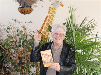 Gerhard Blaboll mit seinem neuen Buch „Rote Erde, heiße Sonne“. Das Coverbild ist eines von zwei Bildern, die Blaboll in Kenia von einem lokalen Künstler erworben hat. 