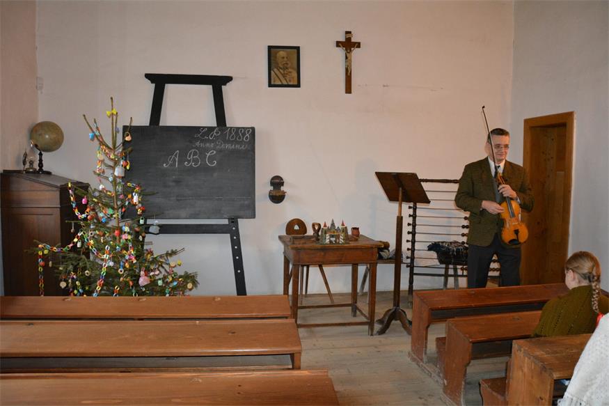 In der Schule des Freilichtmuseums in Rožnov pod Radhoštěm ist es weihnachtlich. Ein Christbaum wurde geschmückt und der Lehrer singt traditionelle Lieder mit den Schülerinnen und Schülern.