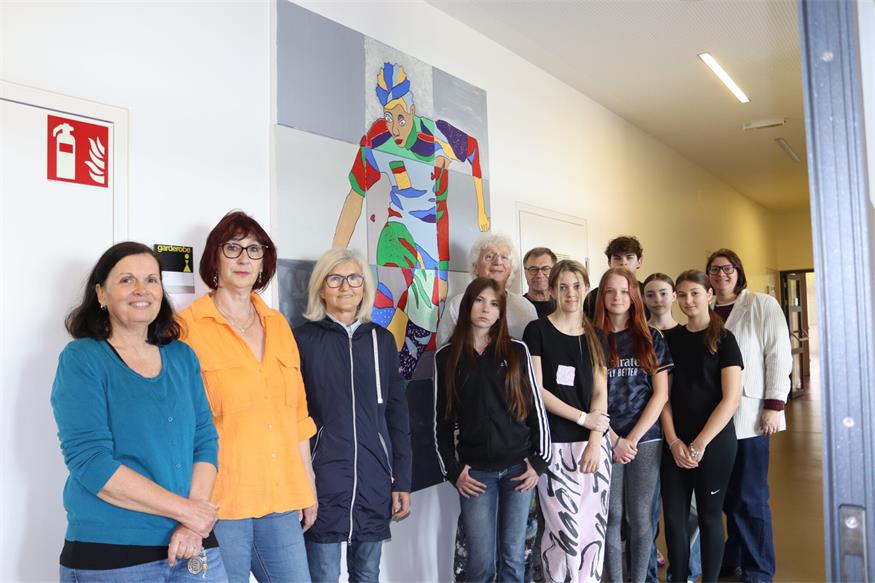 Schülerinnen und Schüler mit Werklehrerin Martina Köppel (l.), Direktorin Carina Werba (r.), den Künstlern Rene Radostics (8.v.r.) und Stefan Blagusz (7.v.r.), Obfrau Eva Messerits (2.v.l.) und Susanne Grössing (3.v.l.) von „Kobersdorf Aktiv“ vor dem fertigen Sportler-Bild. 