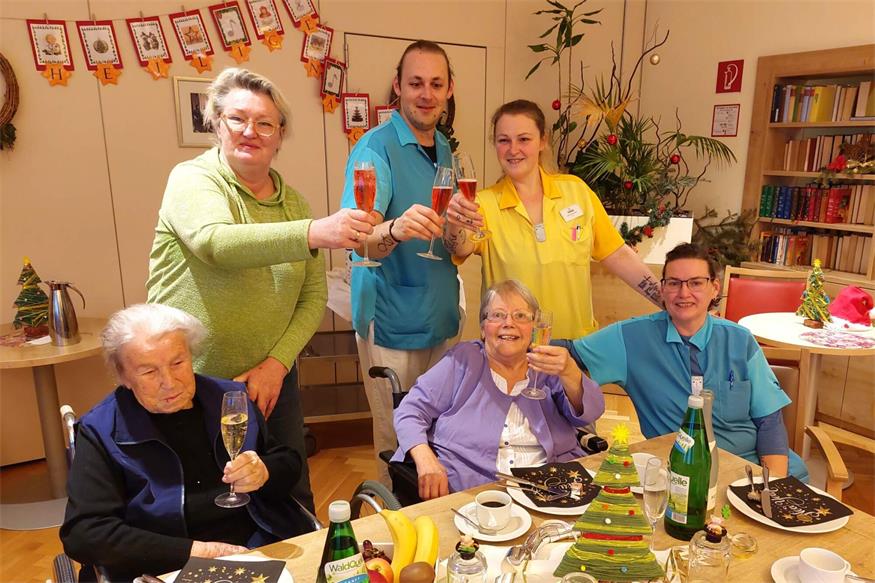 v.l.n.r. (stehend): Wohnbereichsleitung Dominique Jäger, Mitarbeiter Andreas Wieger, Mitarbeiterin Nina Holzbauer, (sitzend): Bewohnerin Anna Seidl, Bewohnerin Maria Bors und Pflegeassistenzleitung Anita Hoffmann stoßen gemeinsam auf das neue Jahr an. 
